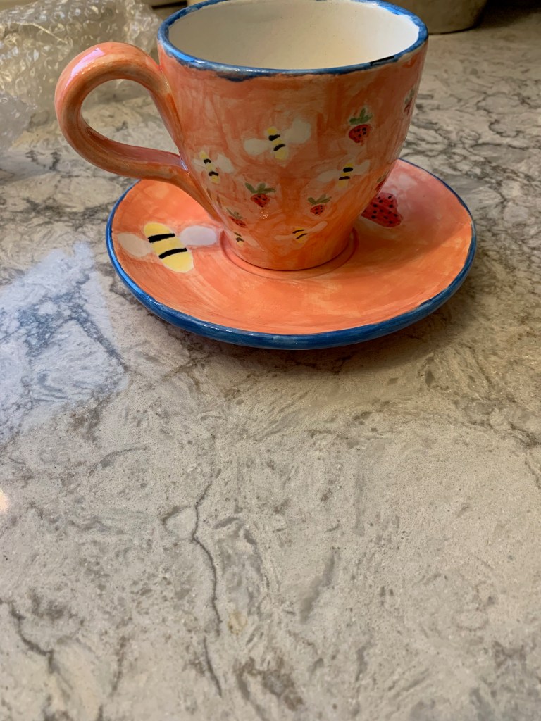 teacup and saucer with bumblebees and strawberries painted on it